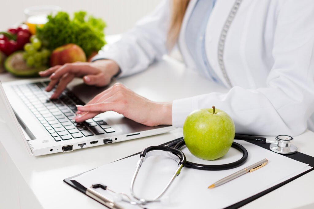 doctor at her desk with fruits and vegetables on the desk working on her computer