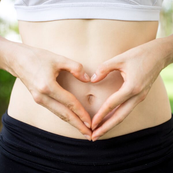 Female hands shaping heart on belly outdoors.