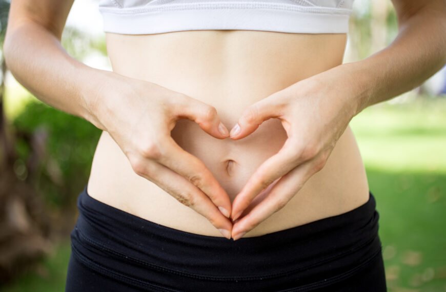 Female hands shaping heart on belly outdoors.