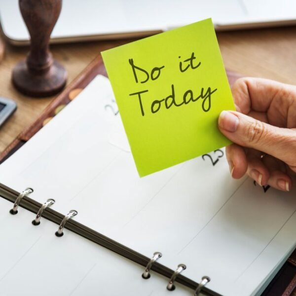 notepad on a table with a hand holding a notes that says do it today. Braking bad habits