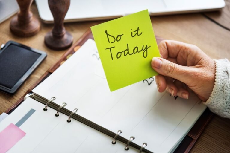 notepad on a table with a hand holding a notes that says do it today. Braking bad habits