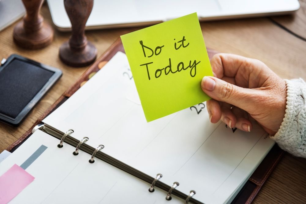 notepad on a table with a hand holding a notes that says do it today. Braking bad habits