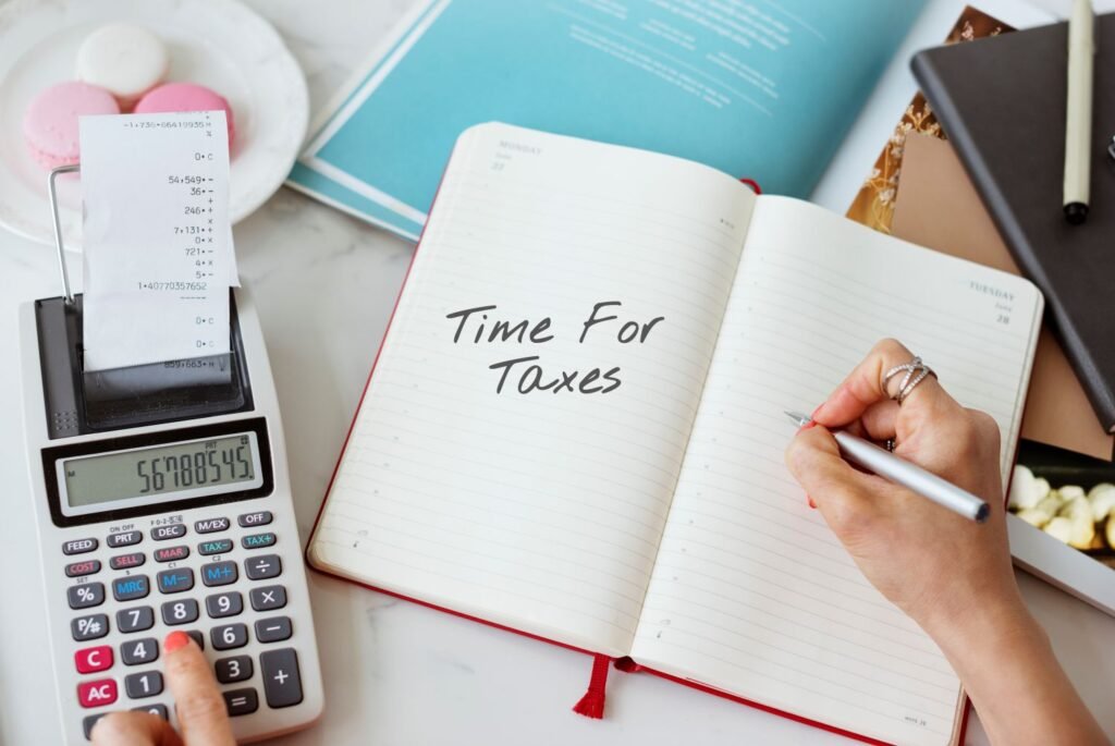A person writing time for taxes in their journal which is on a table next to calculator