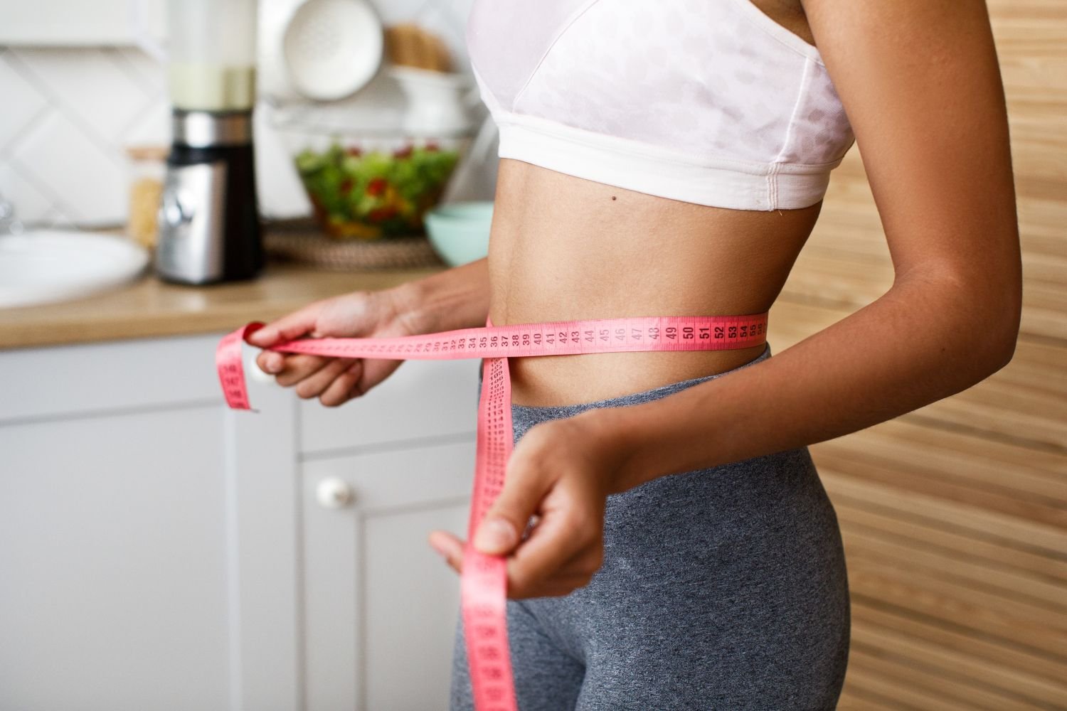 woman in her kitchen measuring her waist