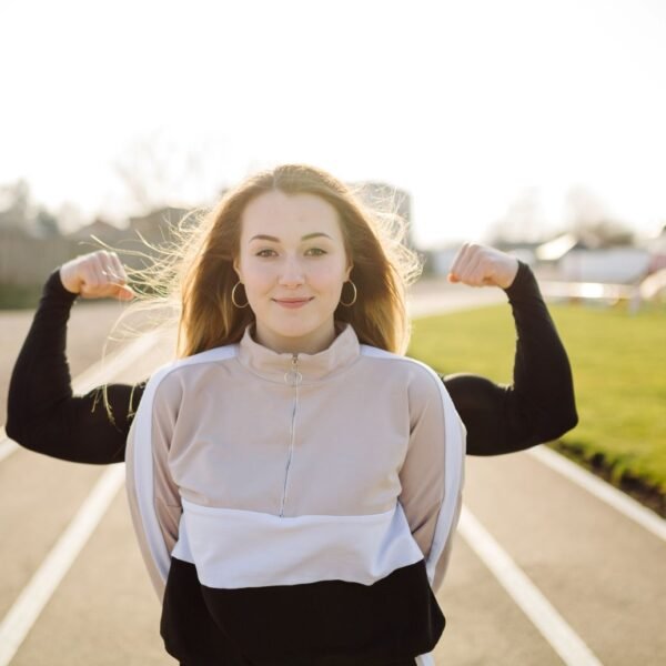 Young woman on a running track field with a person right behind her with raised arms showing their muscles. Mentally strong