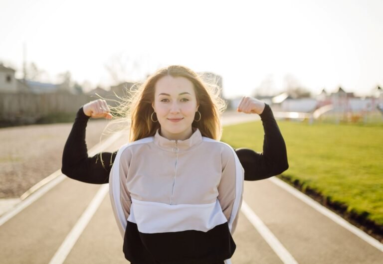 Young woman on a running track field with a person right behind her with raised arms showing their muscles. Mentally strong