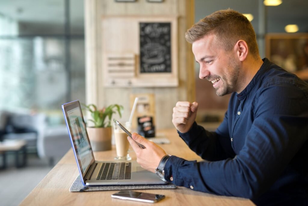 happy young man in front of his laptop holding his cellphone. Using AI to grow his business