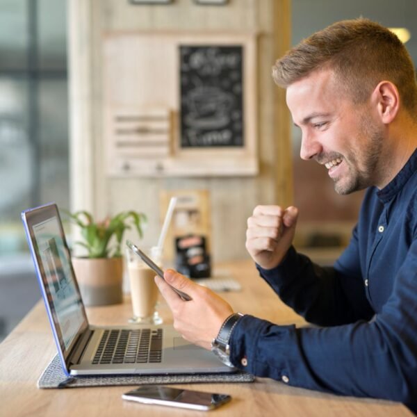 happy young man in front of his laptop holding his cellphone. Using AI to grow his business