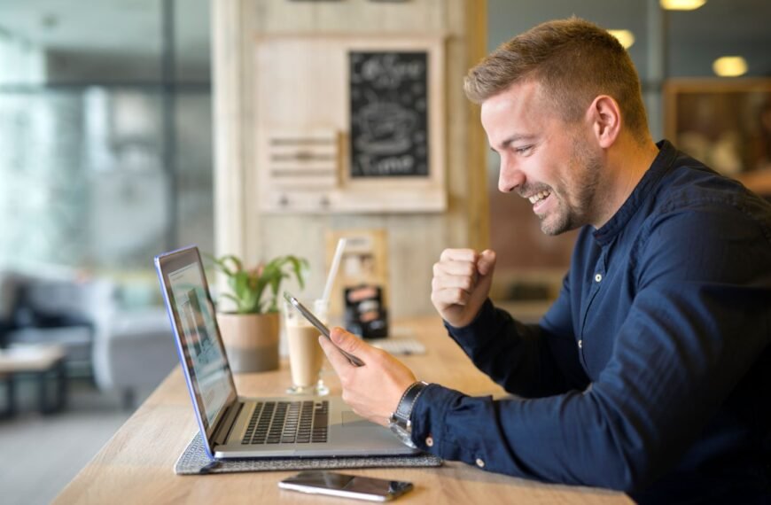 happy young man in front of his laptop holding his cellphone. Using AI to grow his business