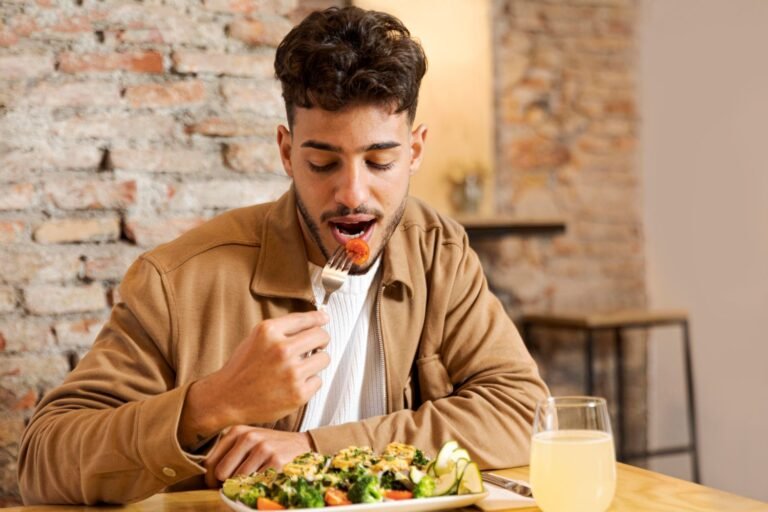 A young man eating a healthy meal in a restaurant with brick wall behind him