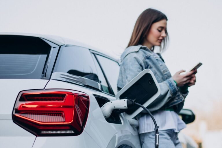Young woman looking at her phone while charging her white electric car