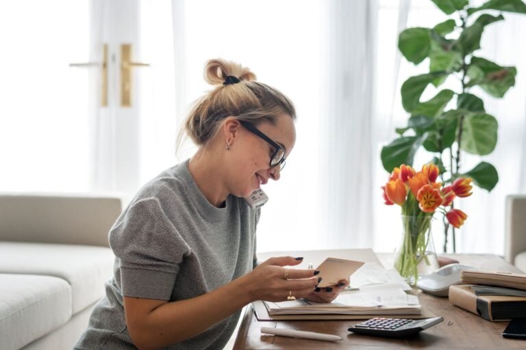 Woman in her living room at her desk talking on a phone and looking at paperwork