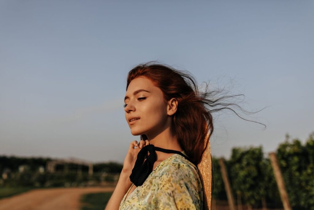 A young woman taking a deep breath outdoors, eyes closed, calm expression — illustrating tools for how to manage stress and anxiety using neuroscience