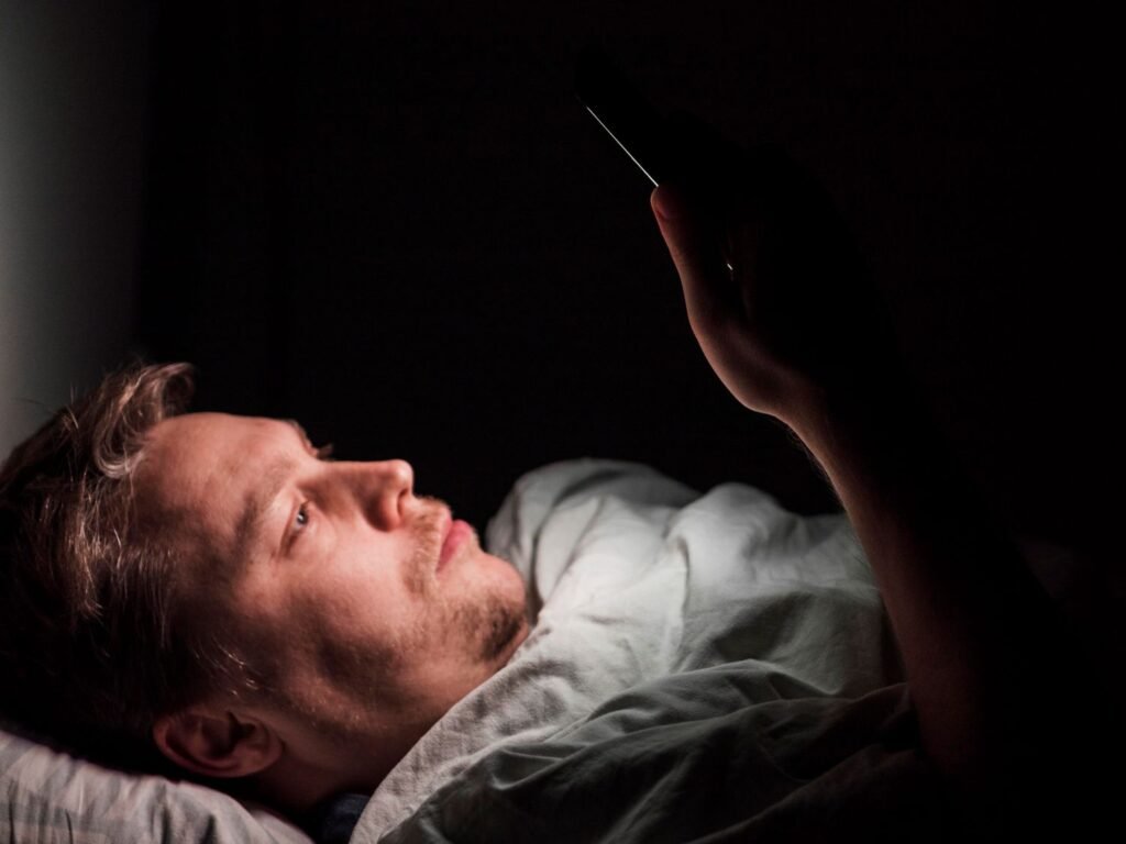 A man looking at a phone late at night with the glow illuminating their face — illustrating digital dopamine addiction and the need to fix dopamine levels