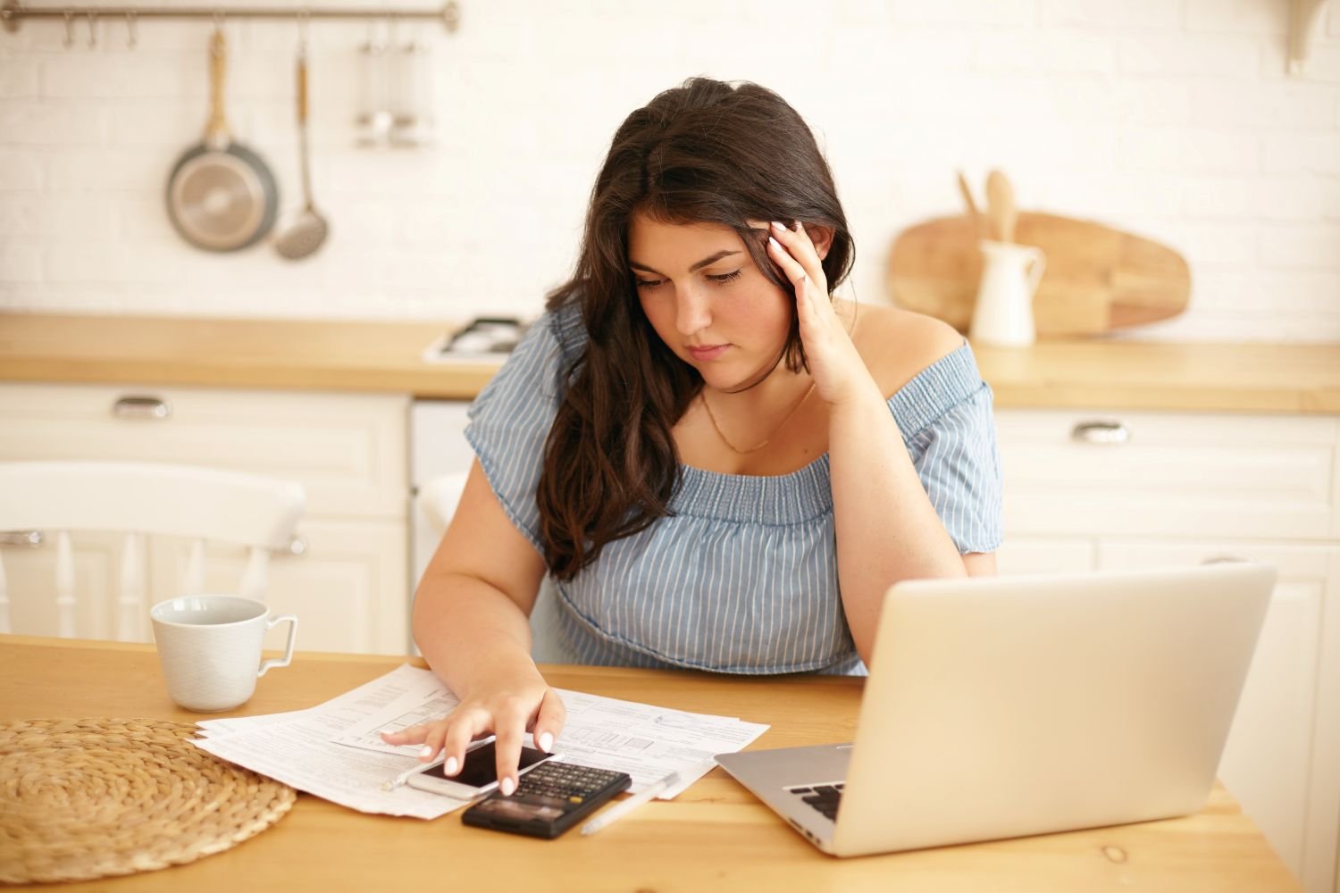 Young woman in her kitchen is looking at her calendar and bills figuring steps to pay of her debt
