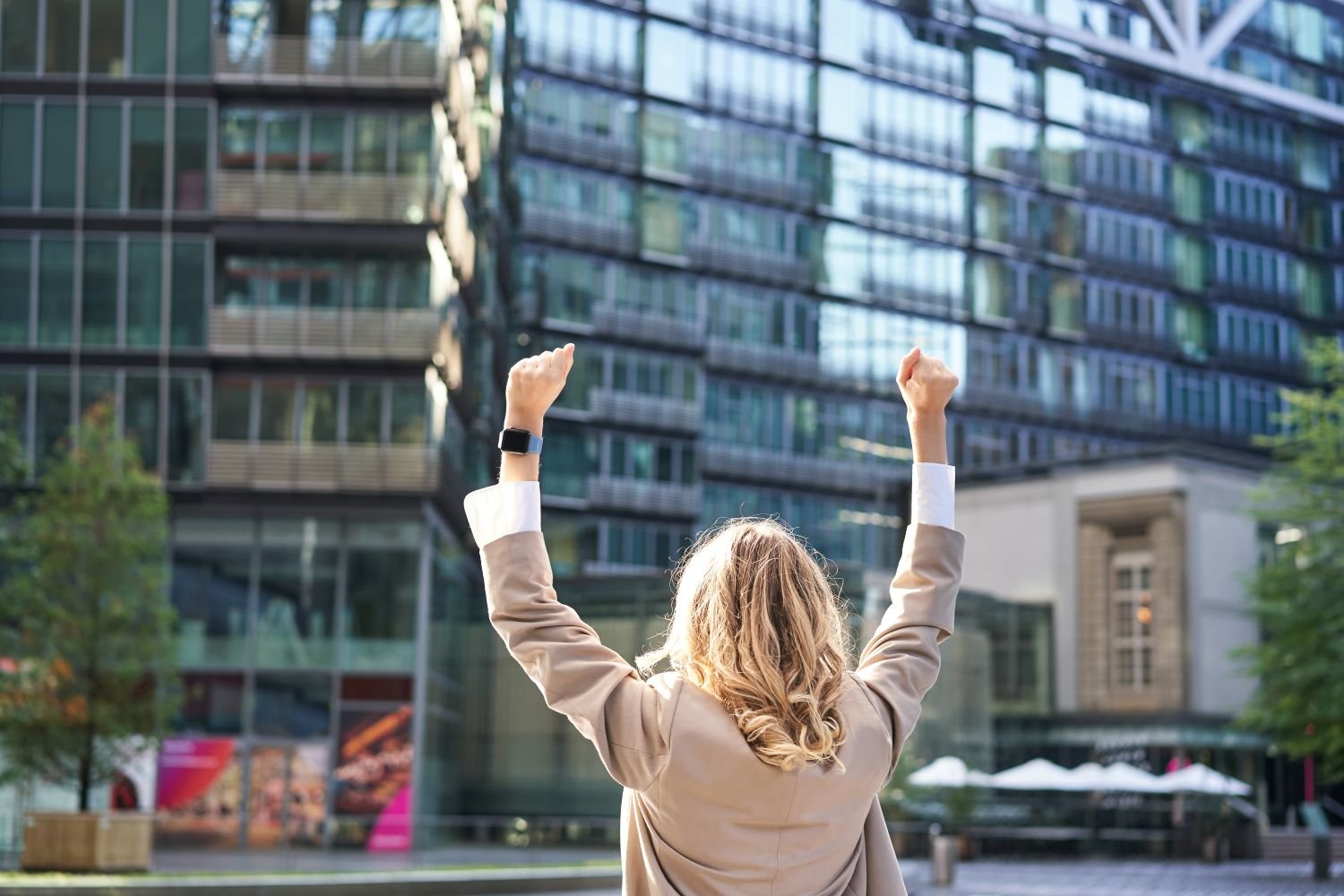 A woman outside in big city with her hands raised enjoys being financially free