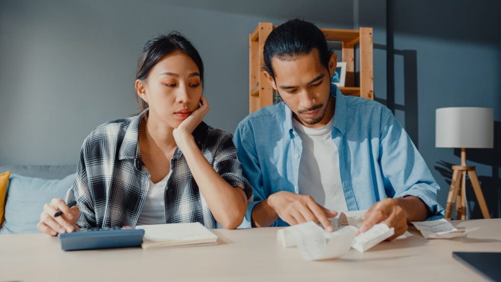 Asian couple in their living room looking at receipts and calculator working on paying off debt
