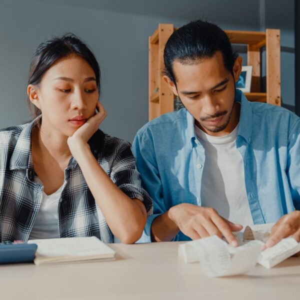 Asian couple in their living room looking at receipts and calculator working on paying off debt