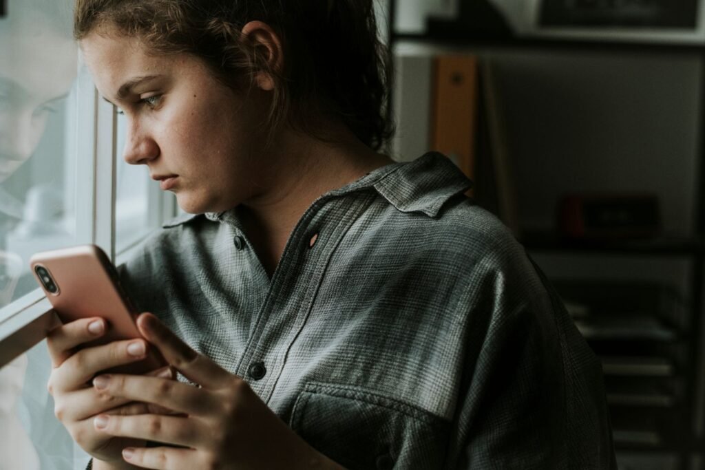 A young sad woman looking out the window while holding her phone
